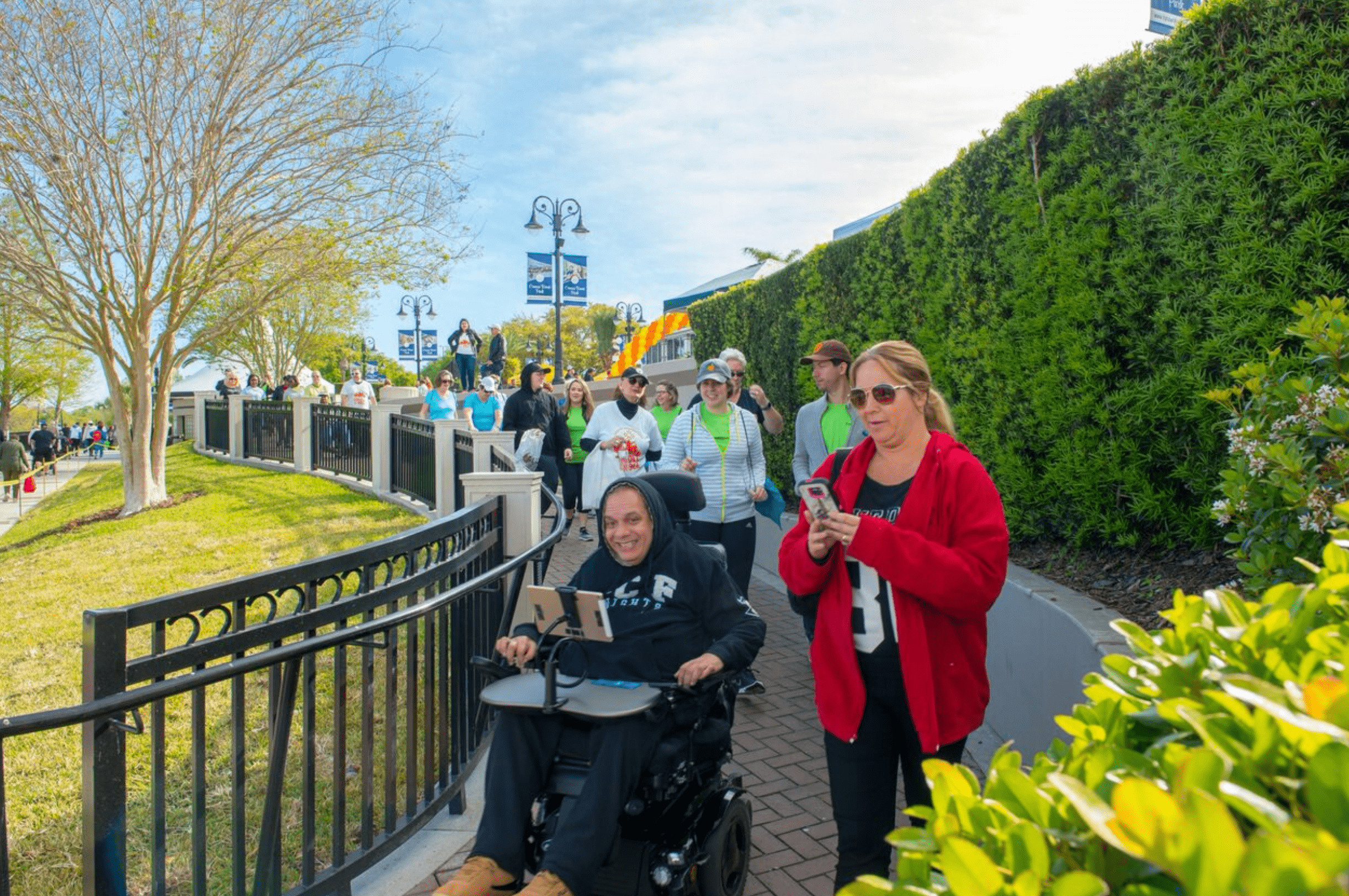 Hector in his electric wheelchair smiling with friends outside on a sunny bright day. 