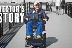 Image of Hector Del Valle in his motorized wheelchair on bridge. Background of photo is black and white and blurred, and Hector is in color. Text to the right of Hector reads "Hector's Story".
