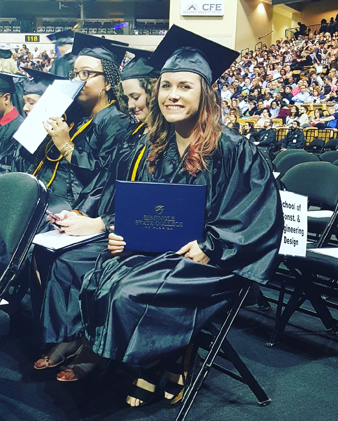 Danielle Head sitting down in graduation gown, smiling and holding diploma.